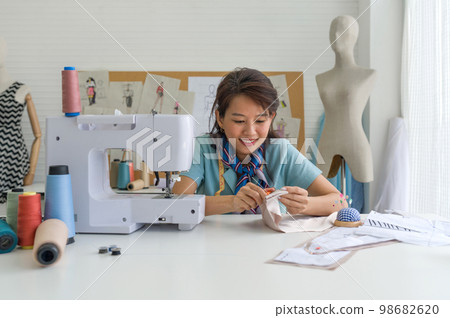 Young dressmaker cut the thread with scissors after finish sewing on a machine. Asian woman working in home base cloth design business. 98682620