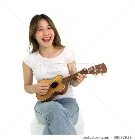 Young asian woman in white t-shirt and jean playing an Ukulele guitar. Portrait on white background with studio light. 98682621