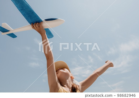 Kid playing with toy airplane. Children dream of travel by plane. Happy child girl has fun in summer vacation by sea and mountains. Outdoors activities at background of blue sky. Lifestyle moment. Kid playing with toy airplane. Children dream of travel by plane. Happy child girl has fun in summer vacation by sea and mountains. Outdoors activities at background of blue sky. Lifestyle moment. 98682946