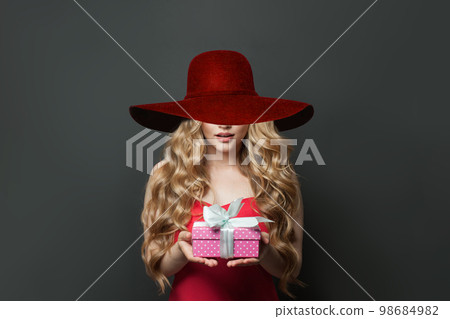 Perfect young woman with gift wearing wide red broad brim hat on black background 98684982