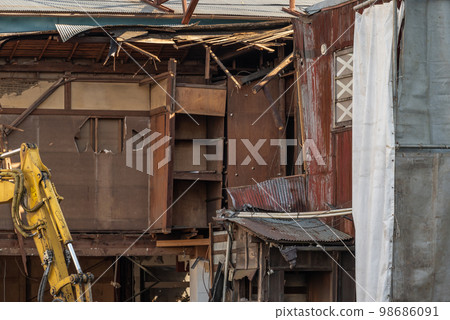 Heavy machinery demolishing an old, vacant wooden house 98686091