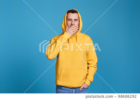 yawning man in yellow sweatshirt on blue background. 98686292