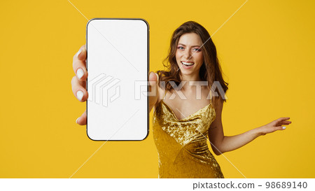 Cheery woman showing modern smartphone with empty screen, advertising new app or website, wearing dress, mockup Cheery woman showing modern smartphone with empty screen, advertising new app or website, wearing dress, mockup 98689140