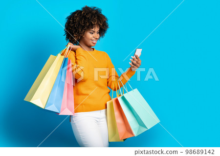 Positive african woman shopping online, using smartphone on blue Positive african woman shopping online, using smartphone on blue 98689142