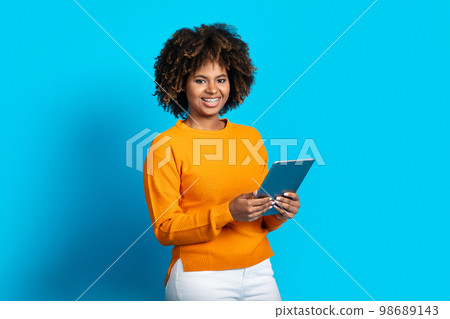 Happy young black woman using pad on blue background Happy young black woman using pad on blue background 98689143