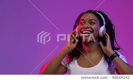 Beautiful Smiling Black Woman Listening Music In Wireless Headphones Under Neon Lighting Beautiful Smiling Black Woman Listening Music In Wireless Headphones Under Neon Lighting 98689242