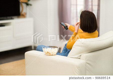Rear view of woman watching TV with popcorn at home Rear view of woman watching TV with popcorn at home 98689514