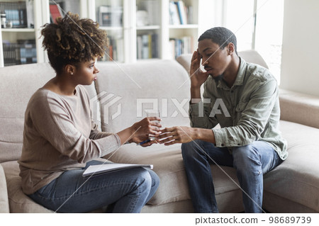 African woman psychotherapist give male patient glass of water 98689739