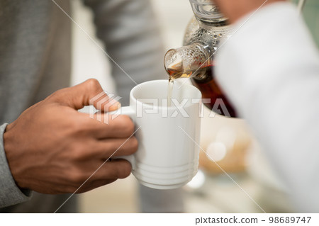 Hands of black woman pouring black tea for her husband 98689747