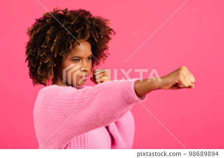 Serious confident young black curly female do hand punch isolated on pink background, close up Serious confident young black curly female do hand punch isolated on pink background, close up 98689894