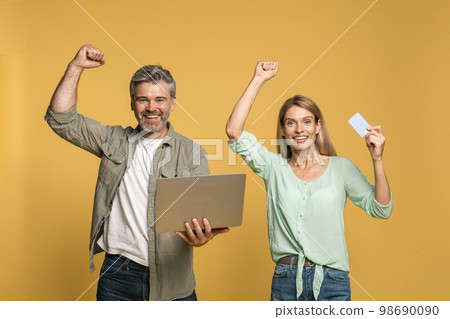 Excited caucasian couple with credit card and laptop making gesture of victory and success, enjoying sales 98690090