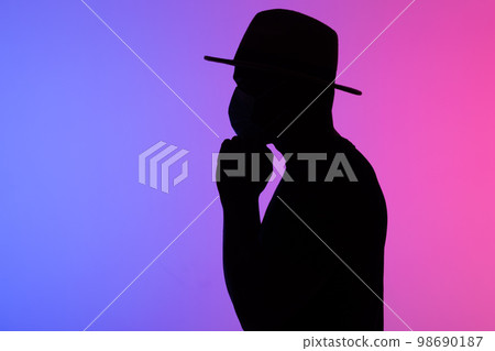 Silhouette african american man in hat with medical mask against the colourful neon background copy space 98690187
