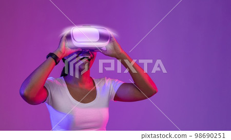 Excited Young African American Woman Wearing Glowing VR Glasses In Neon Light Excited Young African American Woman Wearing Glowing VR Glasses In Neon Light 98690251