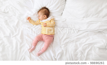 High-angle view of adorable baby girl napping on white blanket on bed during daytime, top view, panorama with copy space 98690261