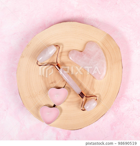 Pink quartz stone massager for face and Guasha scraper, candles as hearts lying on round wooden slice on pink. Anti age, lifting, lymphatic drainage massage, toning treatment. Top view. Square format Pink quartz stone massager for face and Guasha scraper, candles as hearts lying on round wooden slice on pink. Anti age, lifting, lymphatic drainage massage, toning treatment. Top view. Square format 98690519