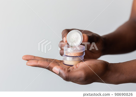 African american man holds mineral facial powder for perfect make-up for women - male make-up artist and cosmetic product concept 98690826