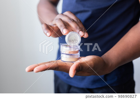 African american man holds mineral facial powder for perfect make-up for women - male make-up artist and cosmetic product concept 98690827
