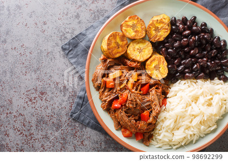 Pabellon criollo is a traditional dish of Venezuela with black beans, rice, plantains and shredded steak that have been cooked with tomatoes closeup on the plate. Horizontal top view Pabellon criollo is a traditional dish of Venezuela with black beans, rice, plantains and shredded steak that have been cooked with tomatoes closeup on the plate. Horizontal top view 98692299