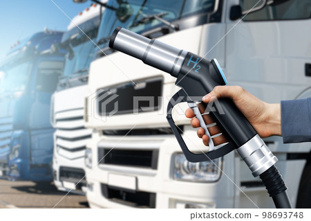Hand with H2 nozzle on a background of hydrogen fuel cell semi trucks. 98693748