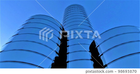 Three abstract round towers of different heights with a glass facade against a blue sky. Bottom view. 3d rendering. Three abstract round towers of different heights with a glass facade against a blue sky. Bottom view. 3d rendering. 98693870