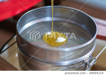 Drop of bee honey drip from hexagonal honeycombs 98694224
