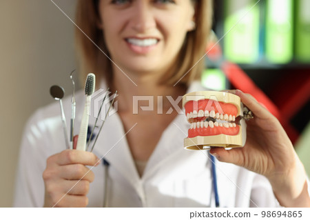 Woman dentist shows medical tools with toothbrush and teeth model. Woman dentist shows medical tools with toothbrush and teeth model. 98694865