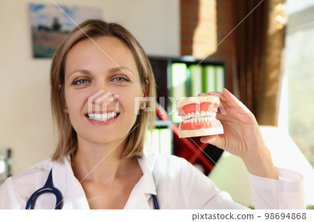 Happy female dentist smiles and holds plastic jaws in her hands close up. 98694868