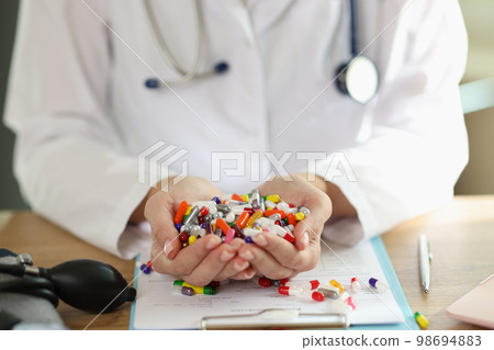 Doctor with stethoscope holds bunch of multi-colored pills in her hands close up. Doctor with stethoscope holds bunch of multi-colored pills in her hands close up. 98694883
