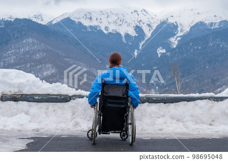 Rear view of a woman in a wheelchair travels in the mountains in winter. Rear view of a woman in a wheelchair travels in the mountains in winter. 98695048