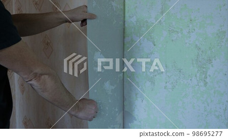 a man rips off a large piece of old paper wallpaper from the wall and copy space on the left on the surface of a texture wall, cleaning room walls from dilapidated wallpaper by hand a man rips off a large piece of old paper wallpaper from the wall and copy space on the left on the surface of a texture wall, cleaning room walls from dilapidated wallpaper by hand 98695277