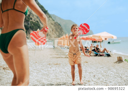 Mom in a green bathing suit and straw sun hat plays with her son on the beach Mom in a green bathing suit and straw sun hat plays with her son on the beach 98695322