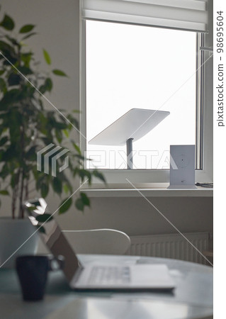 KYIV, UKRAINE - JANUARY 24, 2023: Starlink antenna and wi-fi router on windowsill in home office interior with laptop on table with cup of coffee in foreground, selective focus. KYIV, UKRAINE - JANUARY 24, 2023: Starlink antenna and wi-fi router on windowsill in home office interior with laptop on table with cup of coffee in foreground, selective focus. 98695604