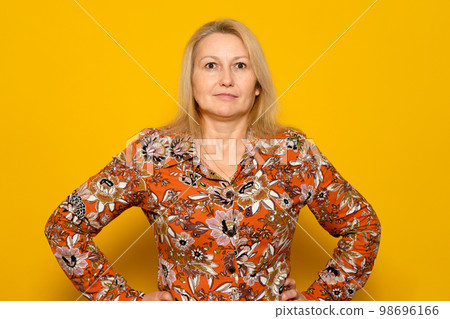 Smiling woman in patterned dress posing isolated on yellow wall background studio portrait. People emotions lifestyle concept. Mock up copy space. Standing with arms akimbo on the waist 98696166