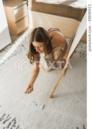 Young woman artist painting on canvas on the easel at home in bedroom - art and creativity concept 98696913