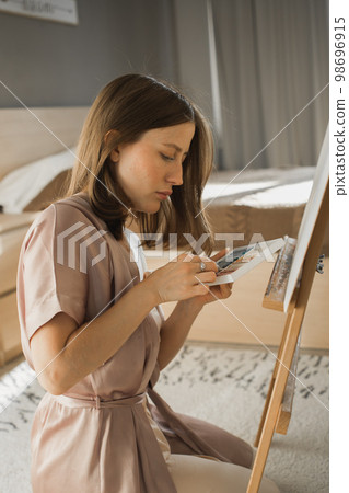 Young woman artist painting on canvas on the easel at home in bedroom - art and creativity concept Young woman artist painting on canvas on the easel at home in bedroom - art and creativity concept 98696915