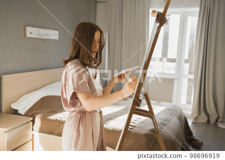 Young woman artist painting on canvas on the easel at home in bedroom - art and creativity concept 98696919
