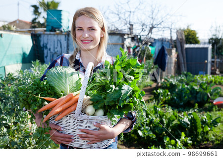 Positive girl with a crop of vegetables on a garden bed 98699661