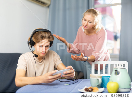 Teenager playing game on phone while upset mother talking to him 98699818