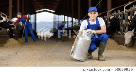 Male farm worker carrying big milk can walking in cowshed on dairy farm 98699939
