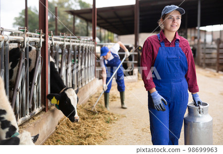 Portraif of caucasian woman dairy farm worker carrying metal milk can in cowshed Portraif of caucasian woman dairy farm worker carrying metal milk can in cowshed 98699963