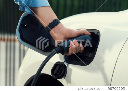 Closeup progressive businessman plugs charger plug from charging station to EV. 98700205