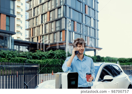 Progressive businessman talking on the phone with recharging electric vehicle. Progressive businessman talking on the phone with recharging electric vehicle. 98700757