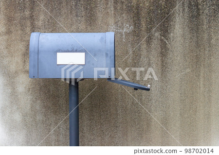 Gray mailbox with open door in front of a concrete wall 98702014