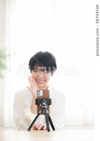 A cute woman streaming videos on her smartphone Vertical A cute woman streaming videos on her smartphone Vertical 98704589