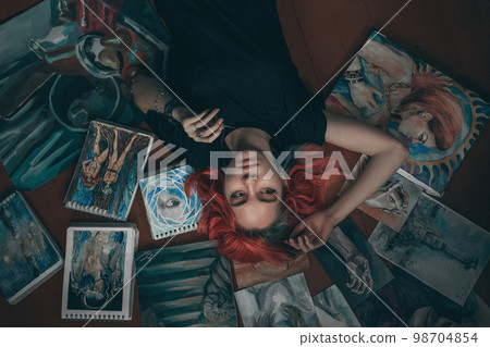 Young redhead woman artist lying on the floor with her paintings. Top view Young redhead woman artist lying on the floor with her paintings. Top view 98704854