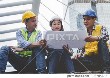 Civil engineer teams meeting working together wear worker helmets hardhat on construction site in modern city. Foreman industry project manager engineer teamwork. Asian industry professional team 98705696