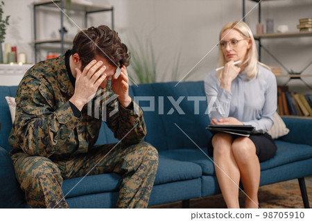 Soldier and psychiatrist sitting on couch during therapy session. Man wearing military uniform. Male warrior with ptds talking to psychiatrist. Soldier and psychiatrist sitting on couch during therapy session. Man wearing military uniform. Male warrior with ptds talking to psychiatrist. 98705910