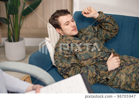 Cropped photo of soldier laying on couch during therapy session. Man wearing military uniform. Male warrior with ptds talking to psychiatrist. 98705947