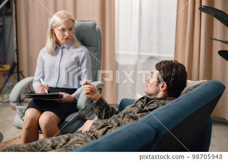 Soldier laying on couch during therapy session. Man wearing military uniform. Male warrior with ptds talking to psychiatrist. 98705948