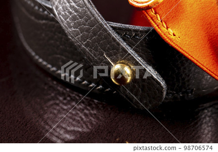 Part of a leather product or belt with a metal rivet on a black background. 98706574